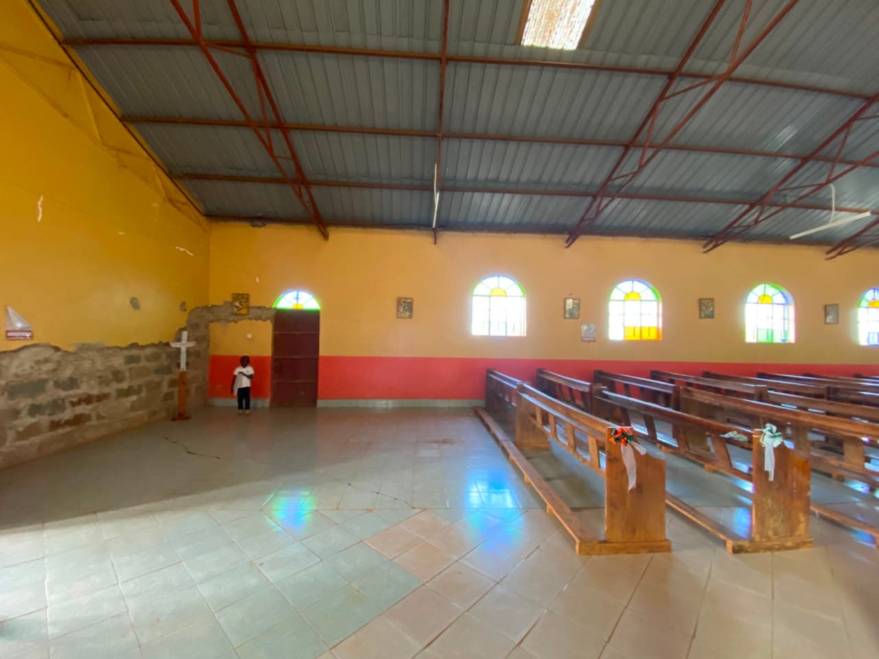 A child stands beside the altar cross near the exposed, unplastered wall.